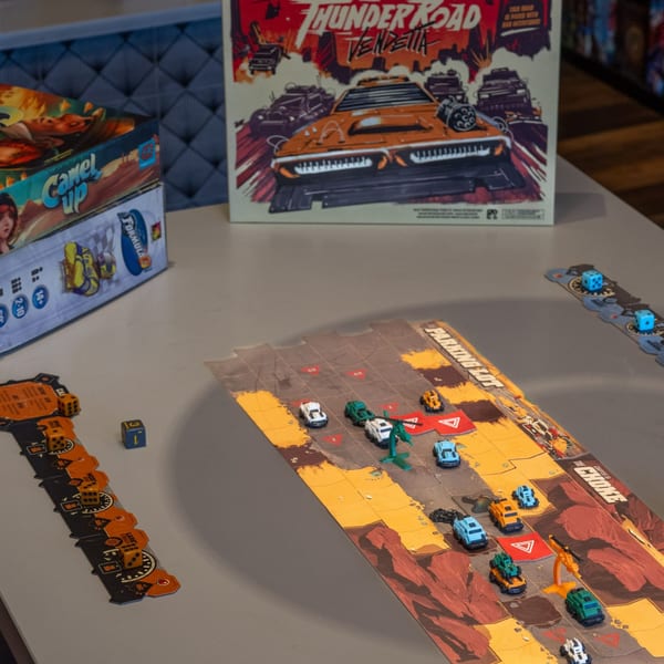 Board games "Thunder Road: Vendetta" and "Camel Up" with game pieces and dice on a table.